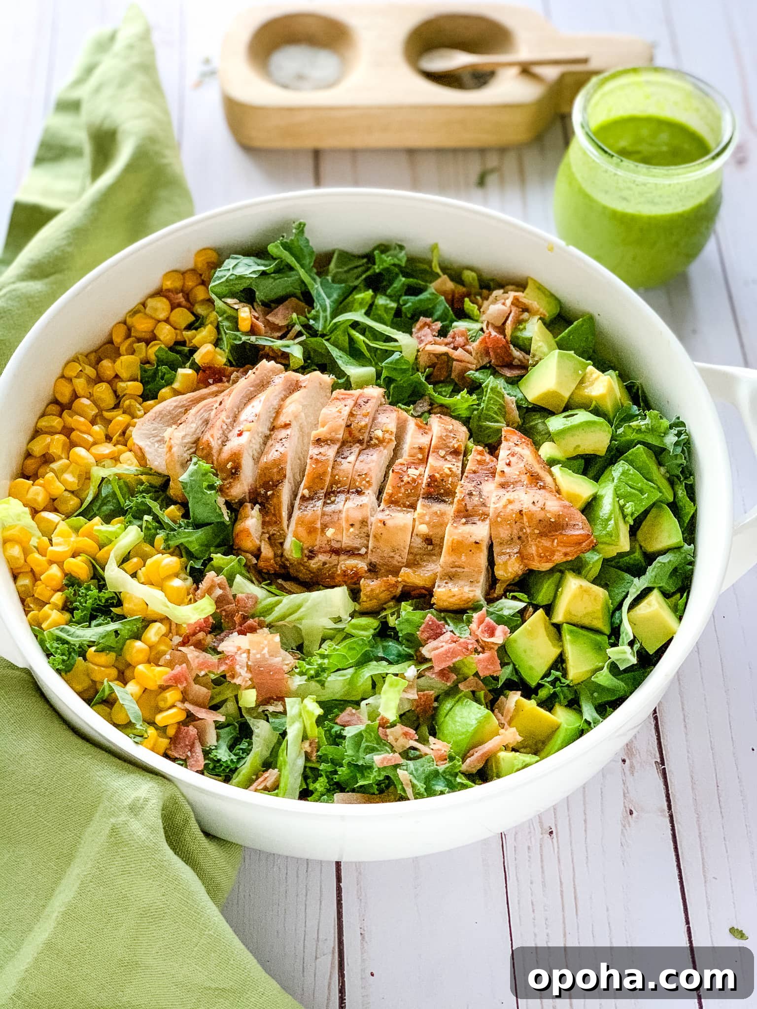 Quick Summer Dinner Recipes for Lazy Weeknights 9 Chicken cobb salad in a white bowl next to a green linen napkin, salt and pepper cellar, and Weck jar of salad dressing.