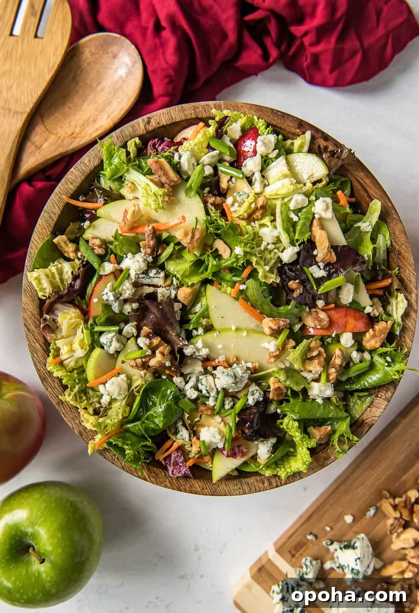 Apple, Walnut & Gorgonzola Cabbage Salad Recipe 2 A top down shot of a cabbage salad with apples, blue cheese, and walnuts, a wooden salad bowl next to a red cloth and salad spoons.