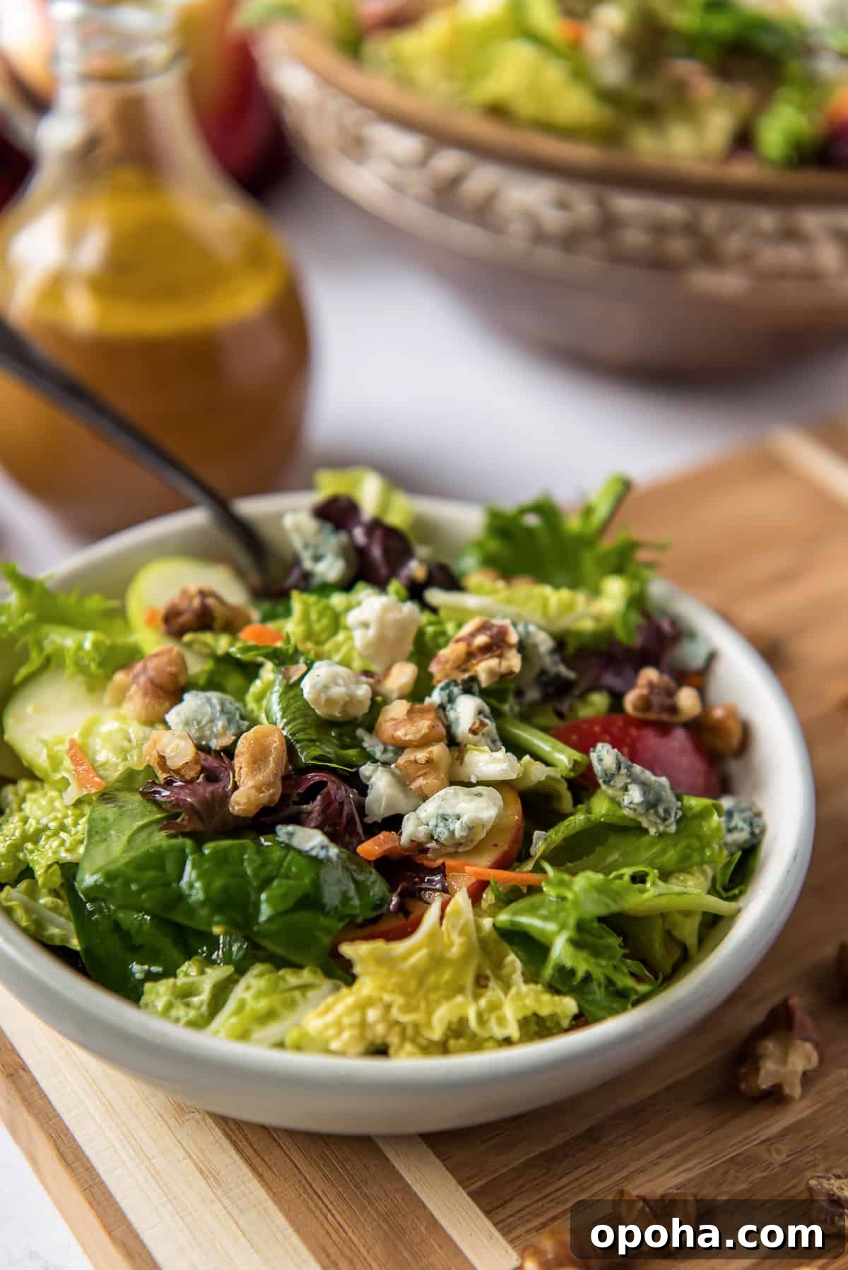 Apple, Walnut & Gorgonzola Cabbage Salad Recipe 3 Cabbage Apple Salad in a white serving bowl on a cutting board with salad dressing behind it.