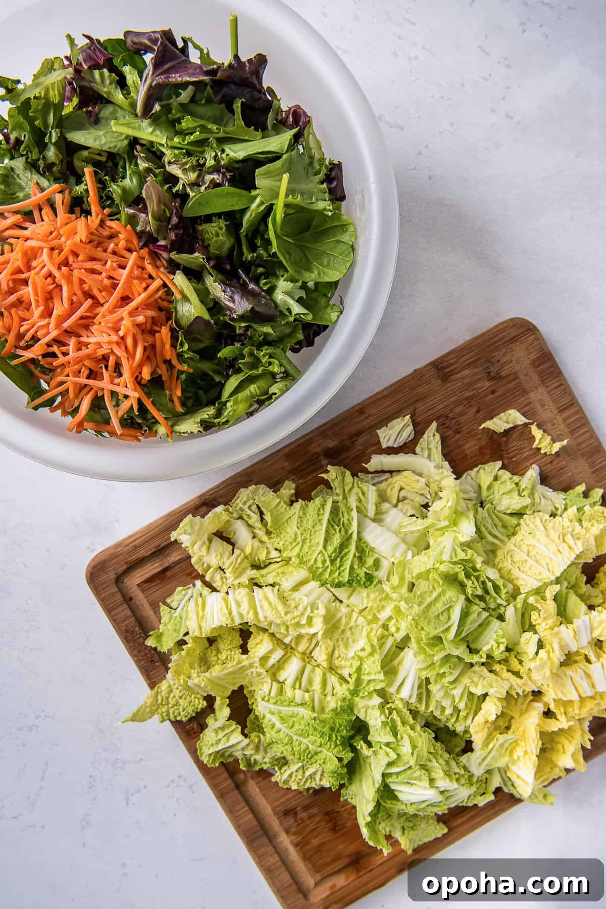 Apple, Walnut & Gorgonzola Cabbage Salad Recipe 5 Chopped cabbage on a cutting board and shredded carrots and spring mix in a salad bowl.