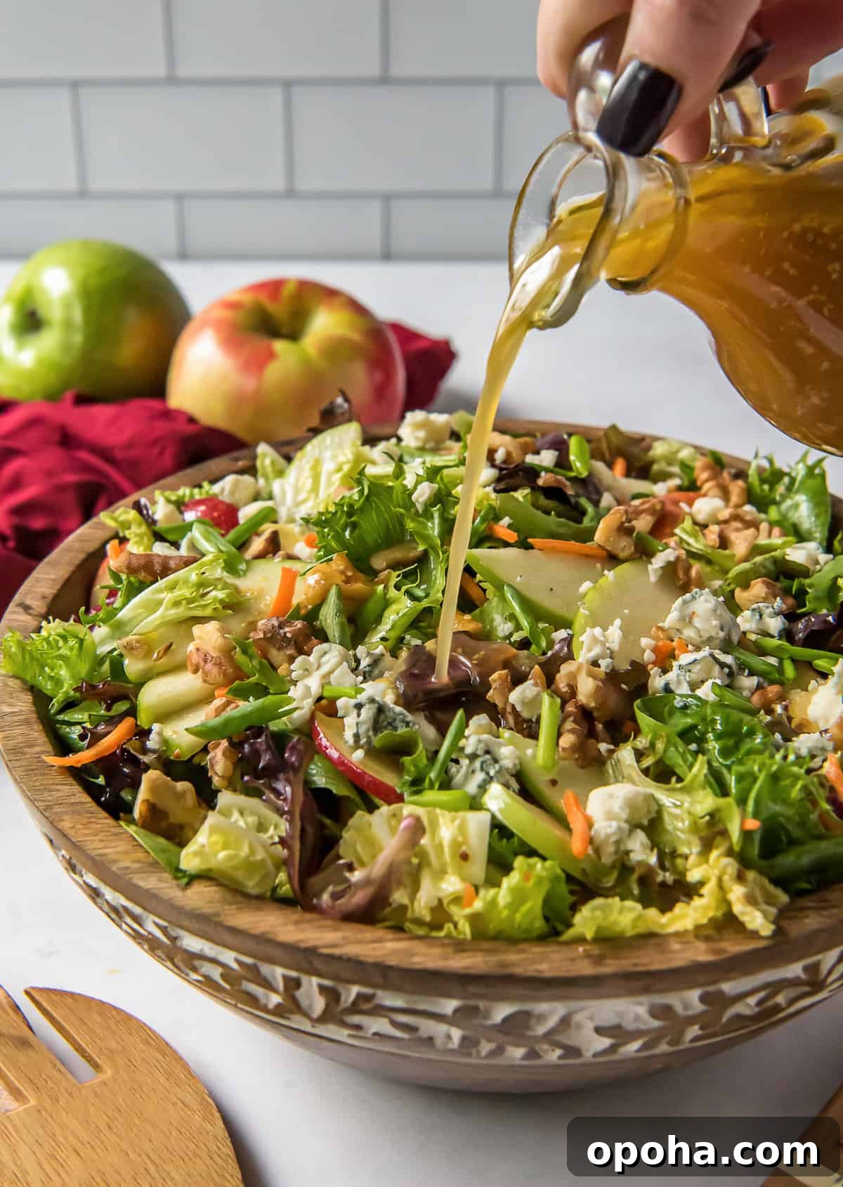 Apple, Walnut & Gorgonzola Cabbage Salad Recipe 6 Salad dressing pours from a carafe on to a salad in a wooden bowl.