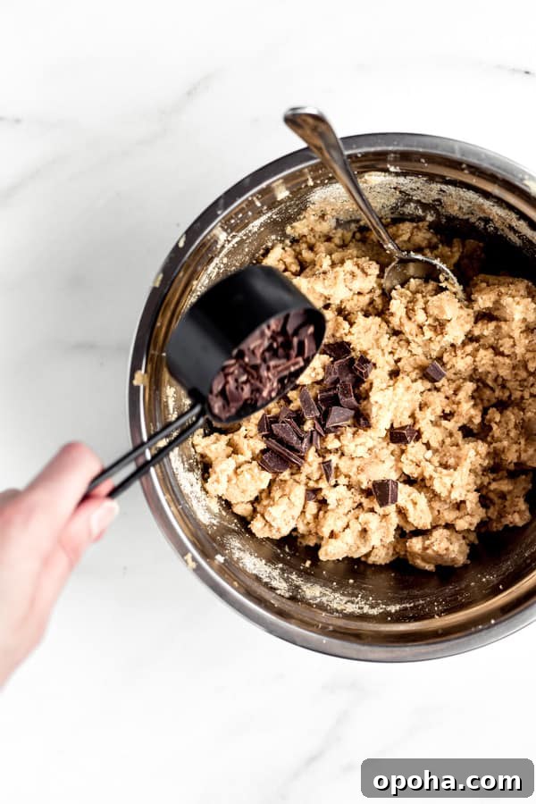 Tahini Blondies (Paleo, Gluten-Free Tahini Brownies) 7 a hand pouring chocolate chunks into a bowl of blondie batter