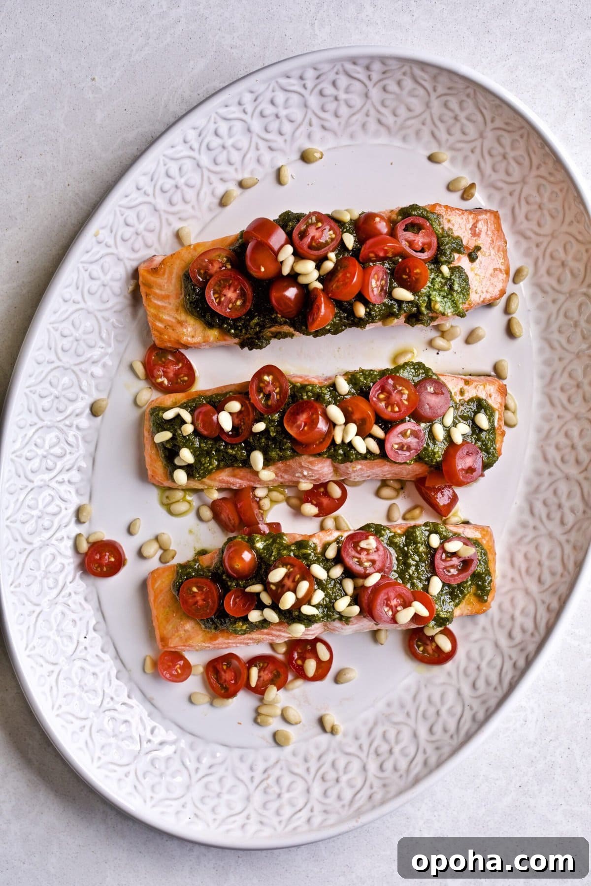 Oven-Baked Salmon with Fresh Basil Pesto 2 Salmon on a plate with pesto, tomatoes, and garnish.