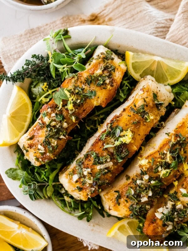 Oven-Baked Salmon with Fresh Basil Pesto 13 Chilean sea bass on a tray with greenery and lemon slices.