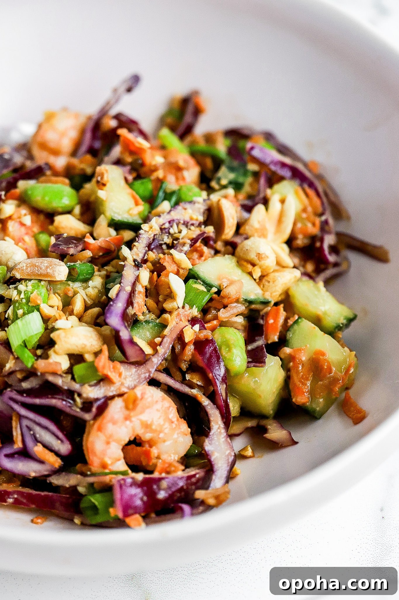 Side view of crispy rice salad in white bowl with peanut dressing and shrimp.