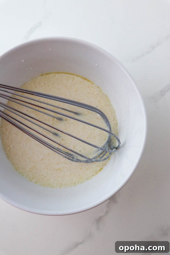 Liquid ingredient for Soft and Tender Buttermilk Bread in a bowl with a whisk.
