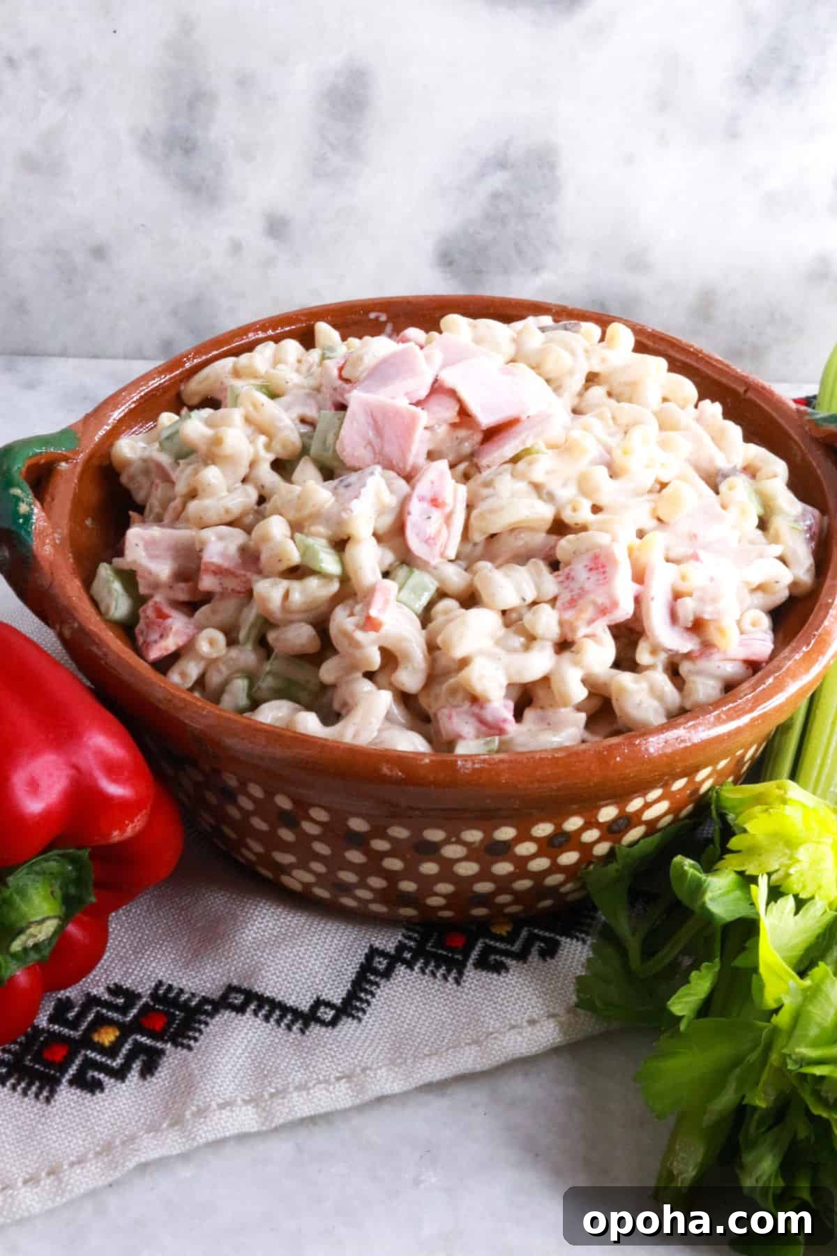 Mexican Macaroni (Ensalada de Coditos) — Creamy Cold Pasta Salad 2 Ensalada de Coditos in a brown bowl with a red bell pepper and stalk of celery beside it.