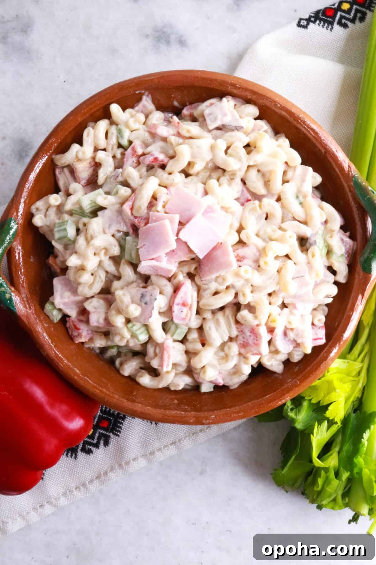 Mexican Macaroni (Ensalada de Coditos) — Creamy Cold Pasta Salad 7 Ensalada de Coditos in a brown bowl with a red bell pepper and stalk of celery beside it.