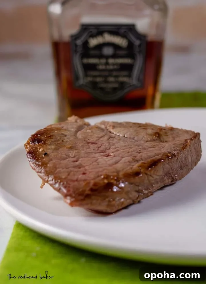 Whiskey Sauce Steak Recipe: Pan-Seared Steak with Rich Whiskey Glaze 3 A piece of pan-seared steak in front of a bottle of whiskey.