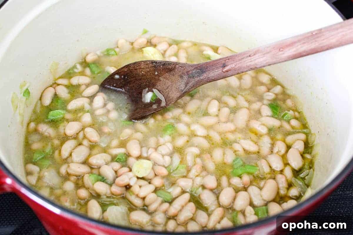 Velvety White Bean Soup with Garlic and Herbs 5 White beans, broth and vegetables in stockpot with wooden spoon.