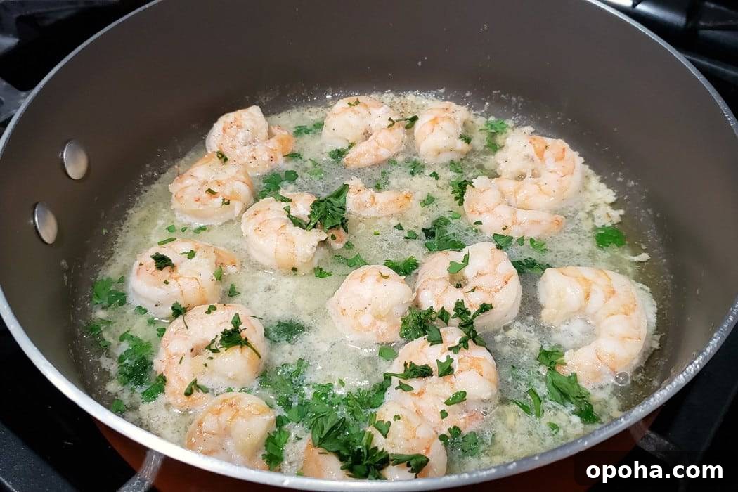 shrimp scampi frying in a pan with fresh parsley.