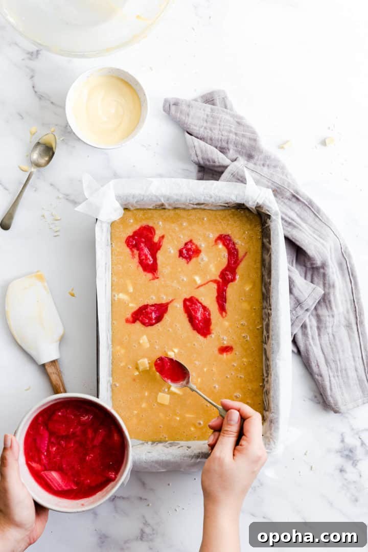 Rhubarb and Custard Blondies Recipe 11 top view of a person adding rhubarb compote on top of cake batter