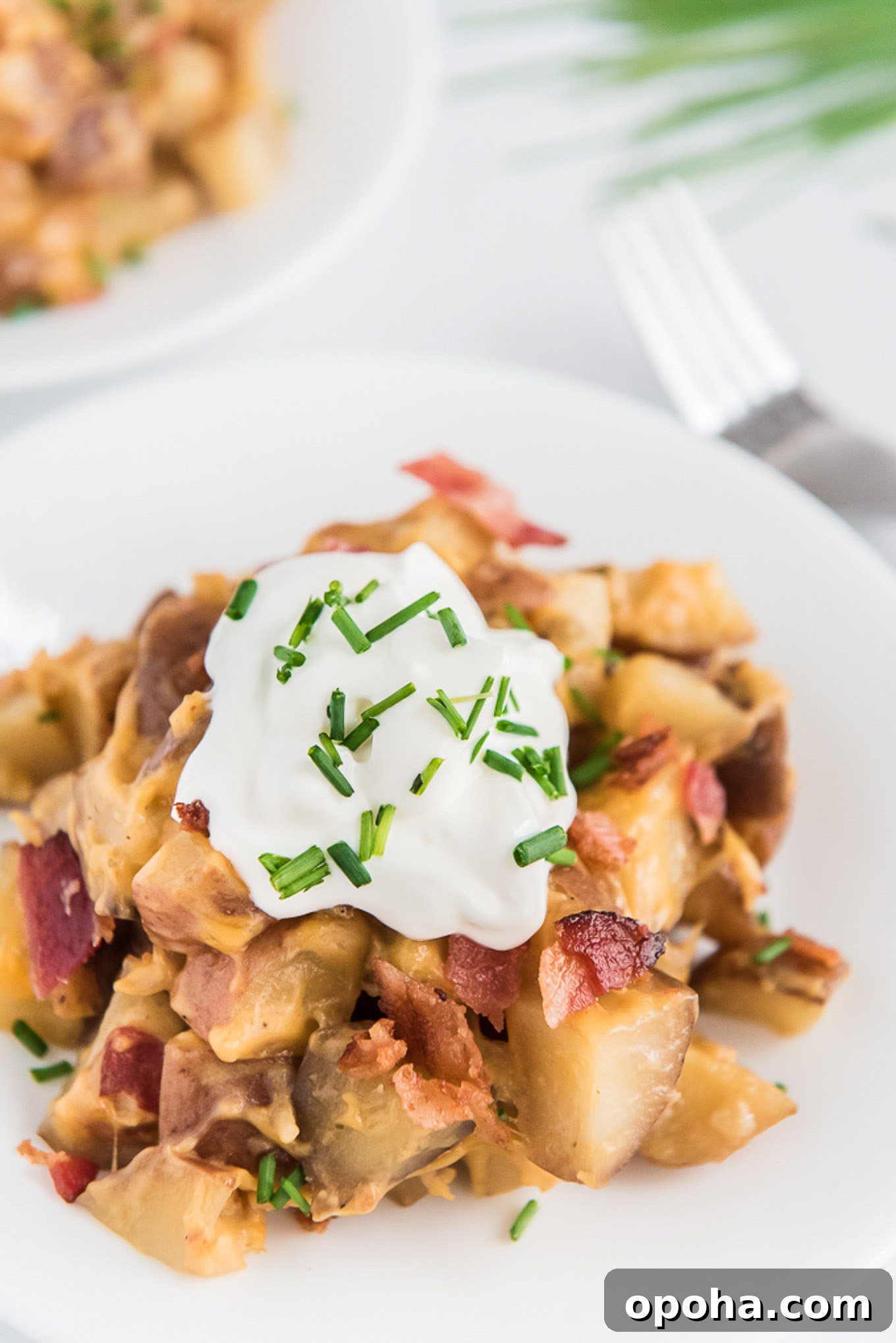 Crockpot cheesy potatoes on a plate topped with sour cream and chives.