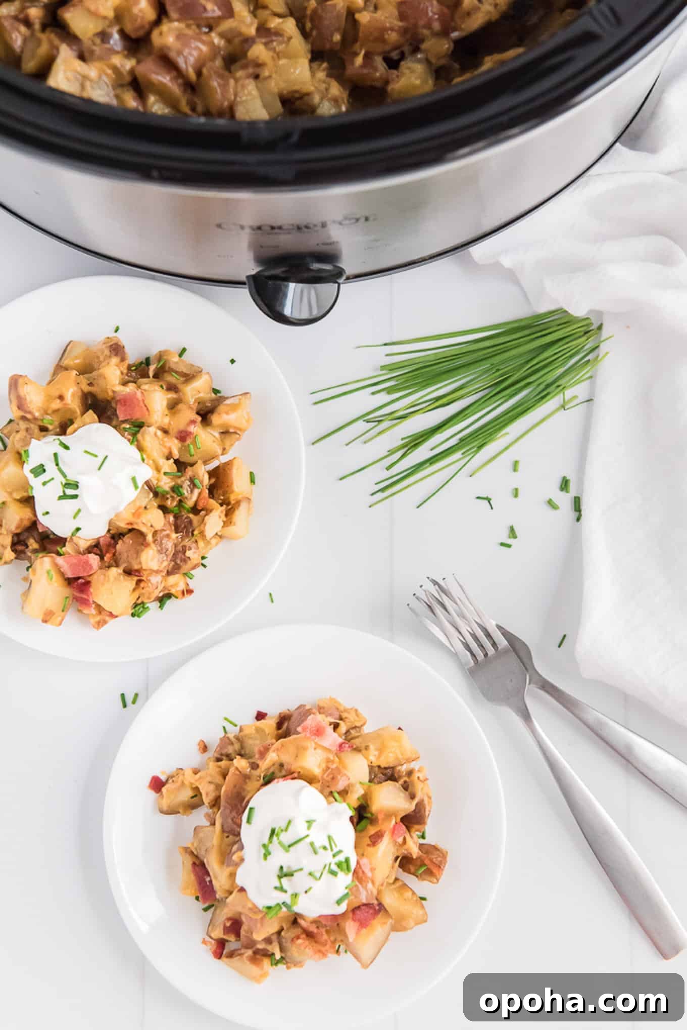 Two plates of slow cooker cheesy potatoes on the table with chives and two forks.
