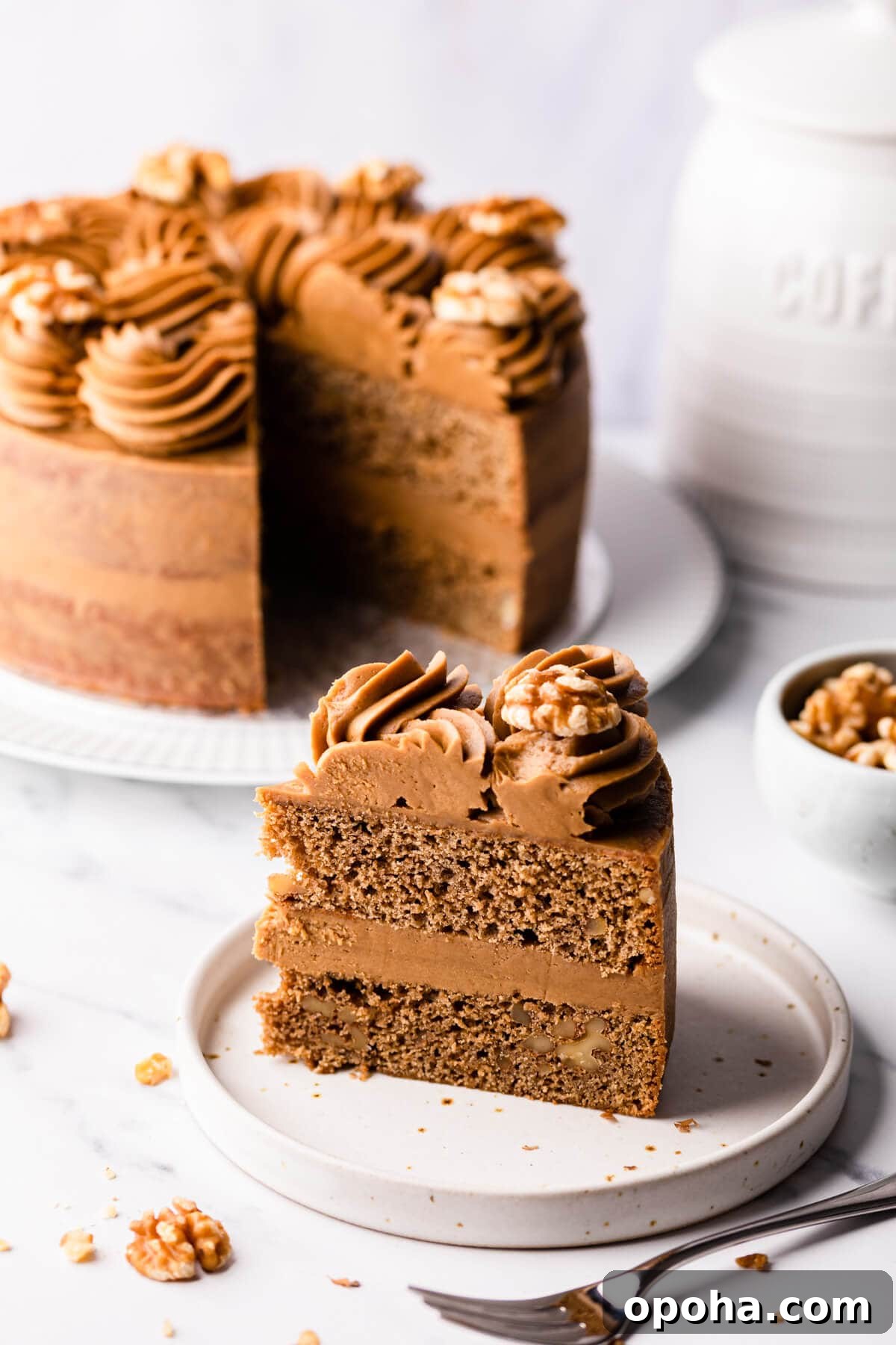 Decadent Coffee and Walnut Cake Recipe for Coffee Lovers 13 slice of coffee walnut cake on a plate with the rest of the cake in the background.