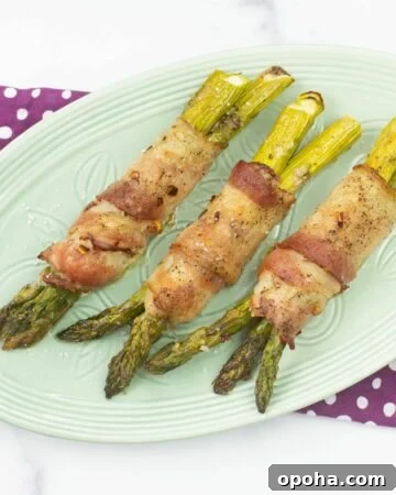 Three bacon wrapped asparagus bundles on a pale green serving plate.