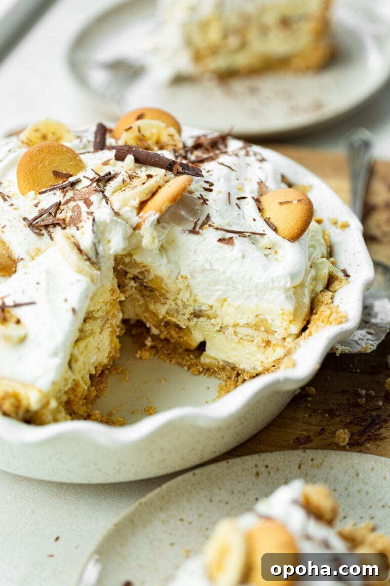 Nilla Wafer Banana Pudding Pie Recipe with Creamy Filling 4 a photo of a thick creamy banana cream pudding pie in a white baking dish with a piece removed so you can see the inside.
