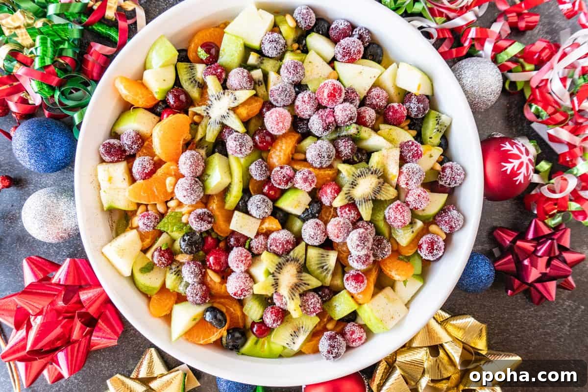 Festive Christmas Fruit Salad with Citrus Pomegranate Dressing 11 Christmas fruit salad in white shallow round bowl with Christmas decorations around it.