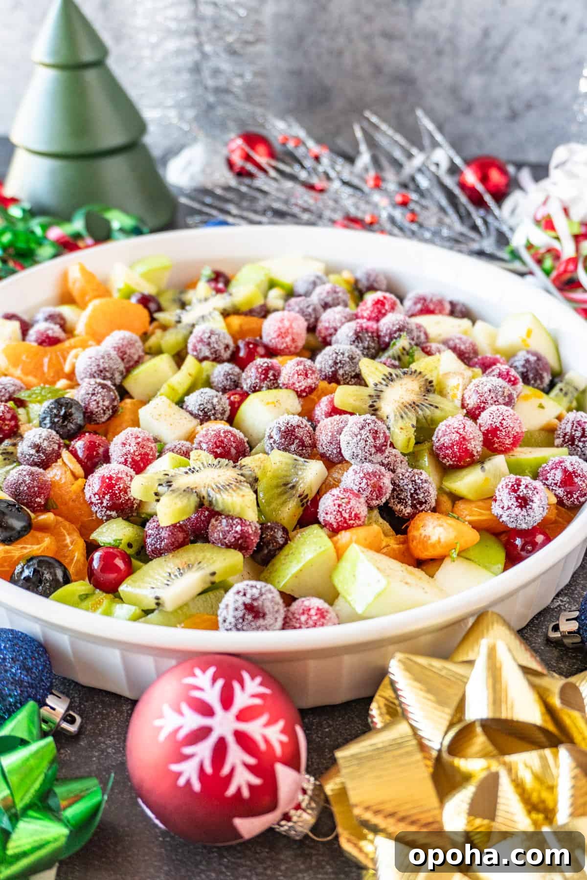 Festive Christmas Fruit Salad with Citrus Pomegranate Dressing 12 Christmas fruit salad in white shallow round bowl with Christmas decorations around it.