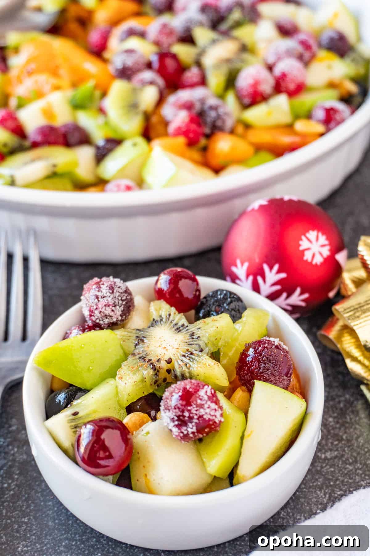 Festive Christmas Fruit Salad with Citrus Pomegranate Dressing 5 Christmas fruit salad in small white bowl, with sugar coated cranberries and a star kiwi on top.