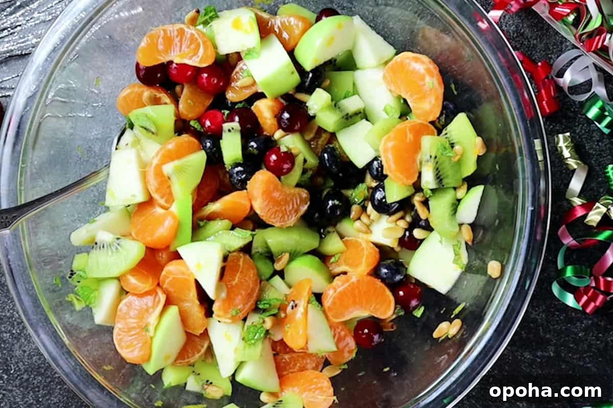 Festive Christmas Fruit Salad with Citrus Pomegranate Dressing 10 chopped fruit mixed in large glass bowl.