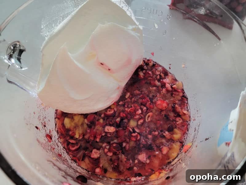Cool whip in a glass bowl on pineapple pieces and shredded cranberries for cranberry salad