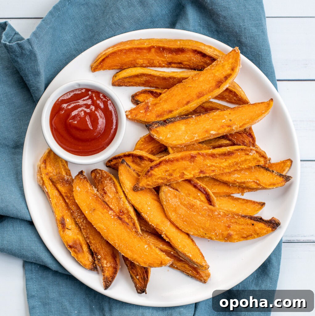 Slow Cooker Sausage and Peppers with Onions and Tomato Sauce 10 Overhead shot of a white plate sitting on blue towel the plate in piled high with crispy sweet potato wedges and a little cup of ketchup.
