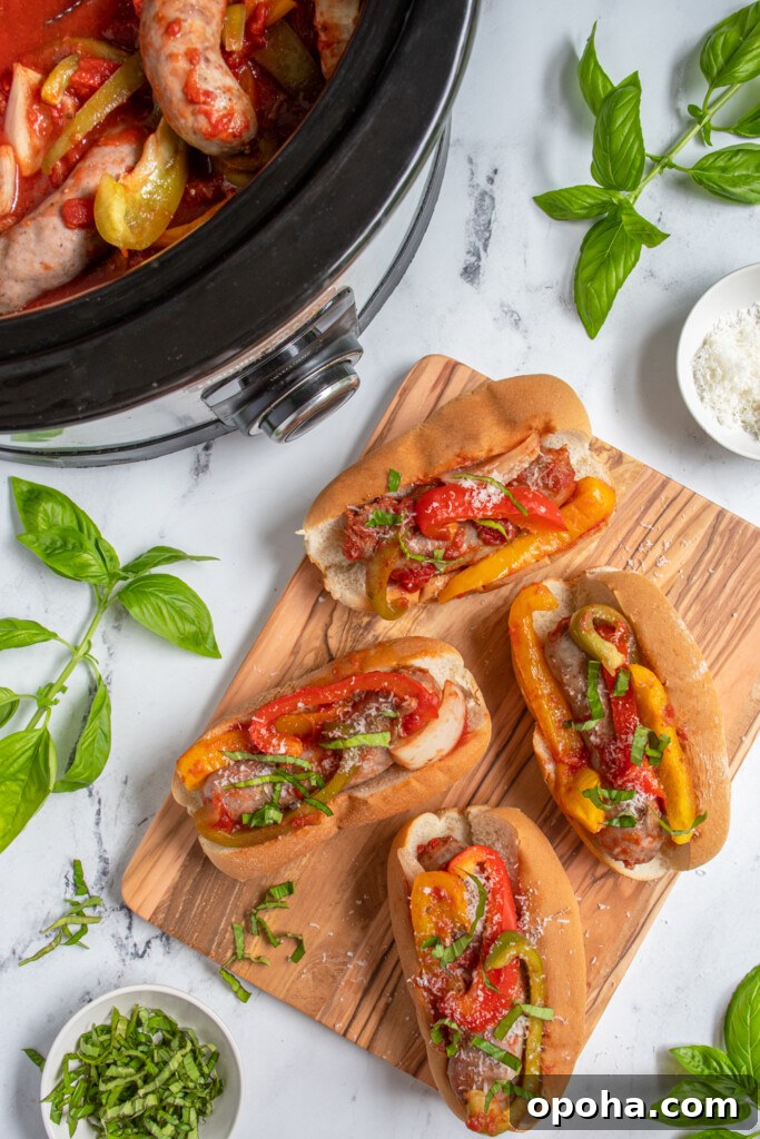 Slow Cooker Sausage and Peppers with Onions and Tomato Sauce 3 Overhead view of a bunch of buns filled with Italian sausages and peppers sitting next to a crockpot with more sausage.