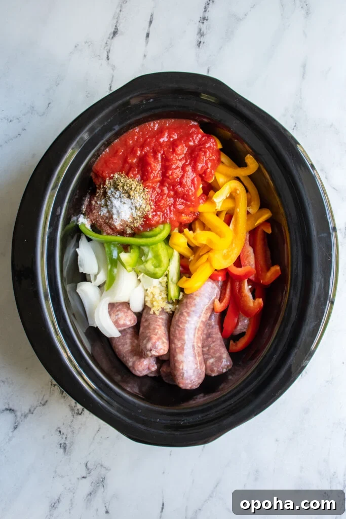 Slow Cooker Sausage and Peppers with Onions and Tomato Sauce 5 Overhead view of a crockpot with uncooked ingredients for sausage and peppers including Italian sausages, sliced bell pepper, and crushed canned tomatoes.