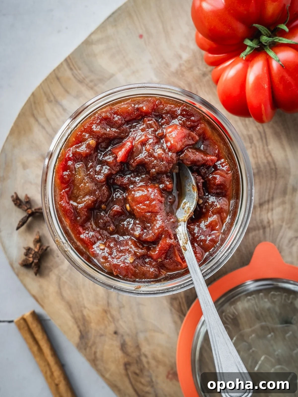 A mason jar filled to the top with tomato jam, sitting on a wooden board.