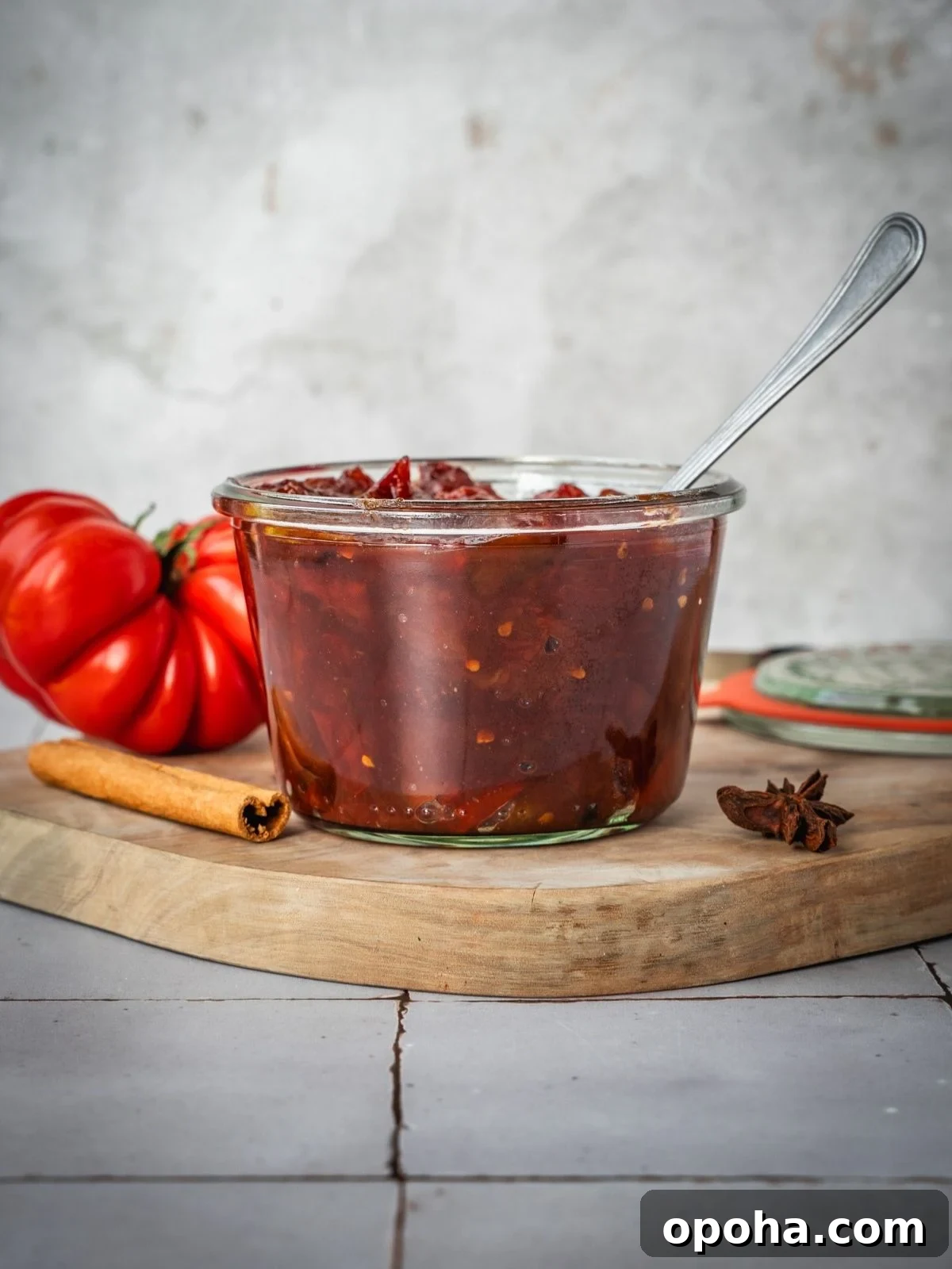 A mason jar filled to the top with tomato jam, sitting on a wooden board.
