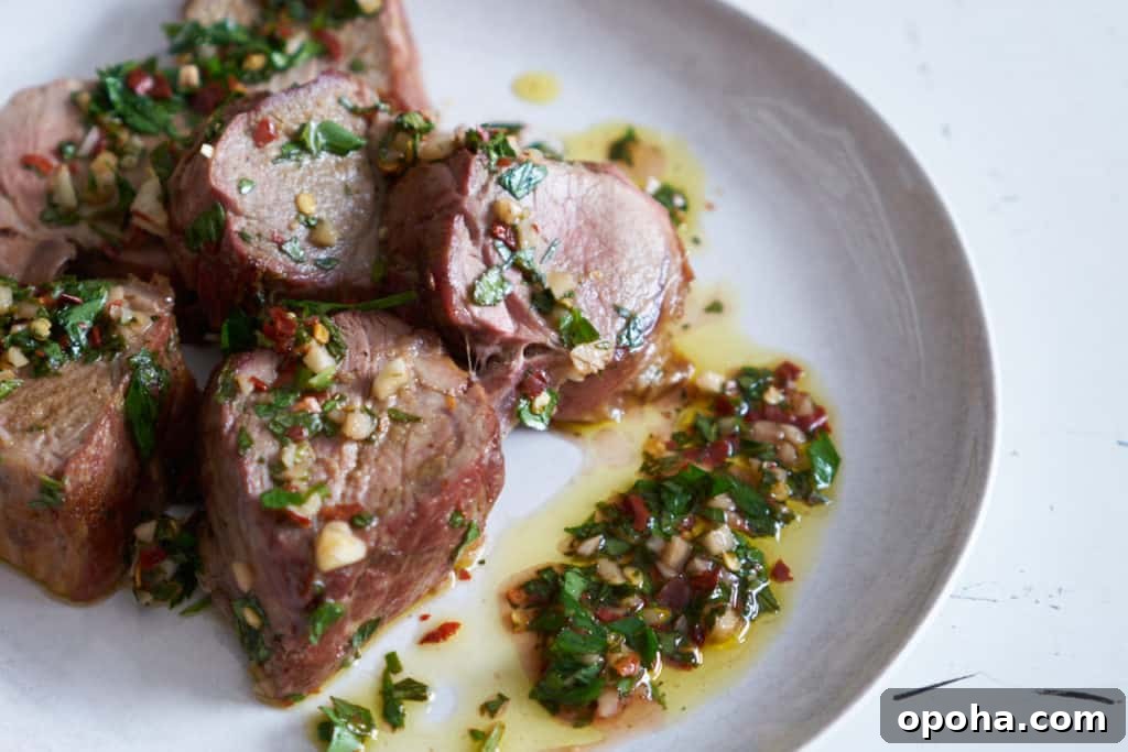 Slices of grilled pork tenderloin with chimichurri sauce on a white plate.