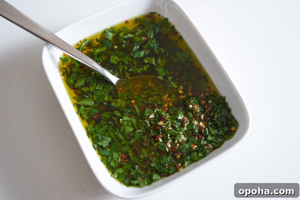 Chimichurri sauce in a white rectangular bowl with a spoon in it.