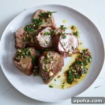 Slices of grilled pork tenderloin with chimichurri sauce on a white plate.