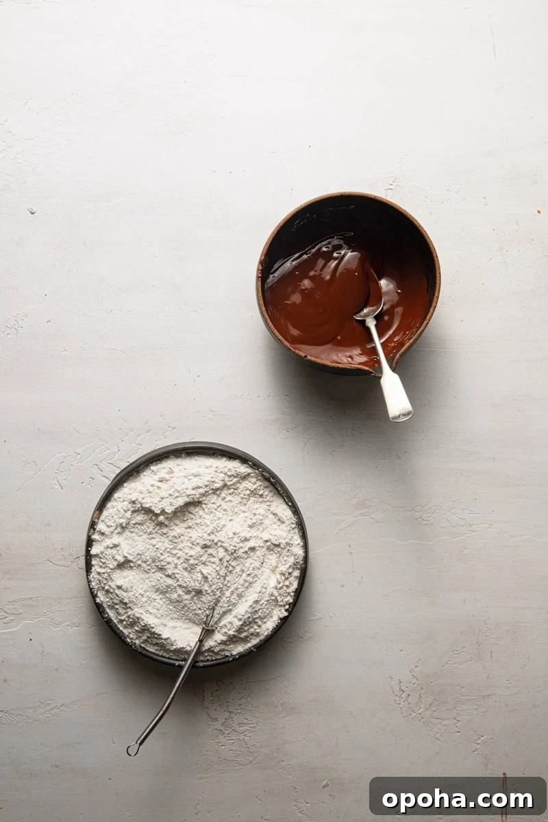 A bowl with melted chocolate next to a bowl with flour.