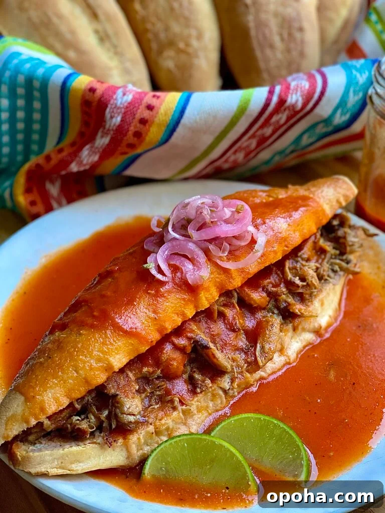 A mexican sandwich called torta ahogada, with carnitas and refried beans inside a crusty birote salado, drowned in a spicy tomato salsa. topped with pickled red onions with some lime wedges on the side. 