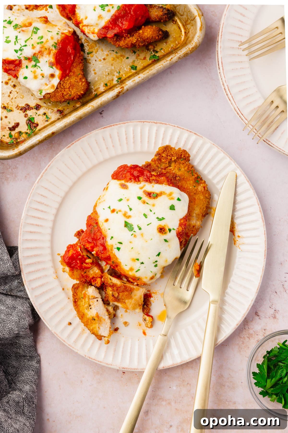 Crispy Gluten-Free Chicken Parmesan Recipe for Dinner 5 A piece of Gluten-Free Chicken Parmesan on a plate with a fork and knife.