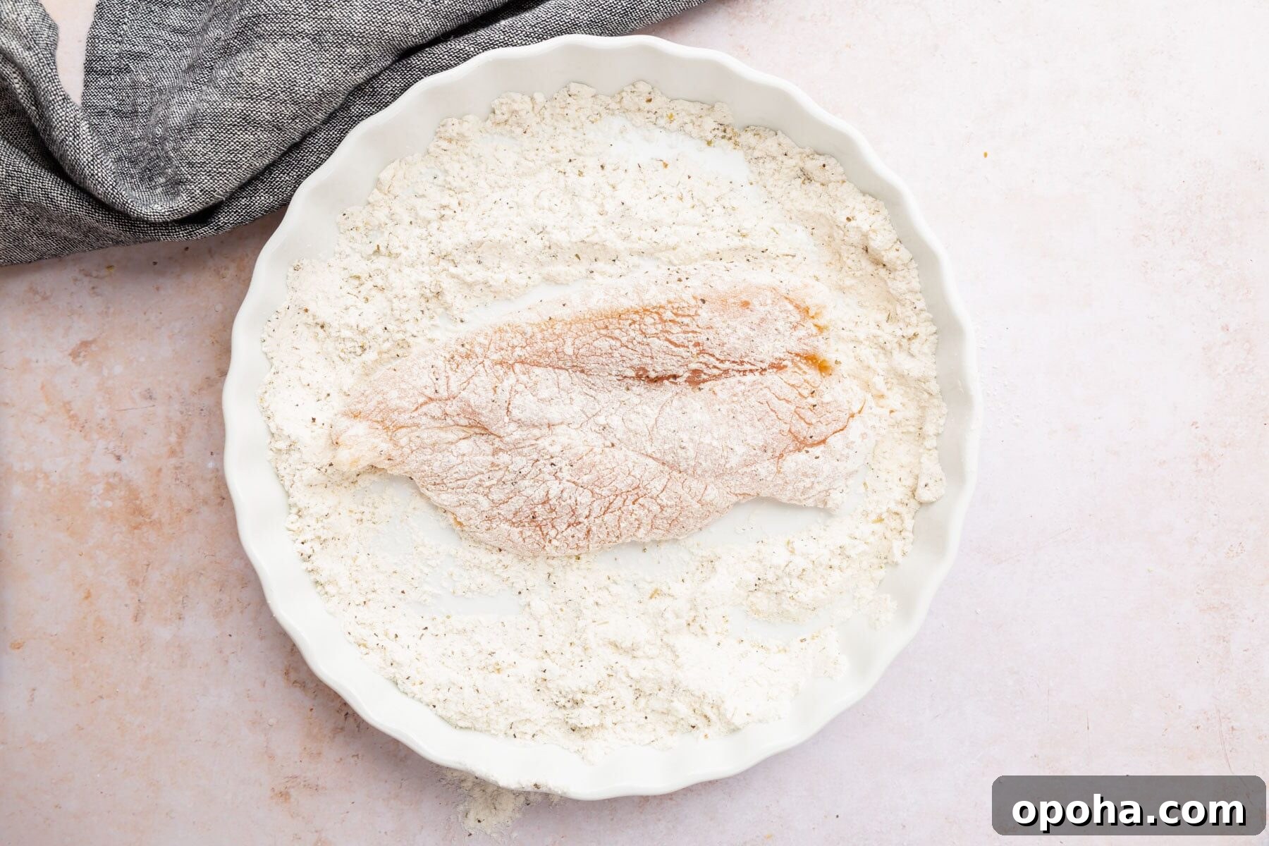 Crispy Gluten-Free Chicken Parmesan Recipe for Dinner 9 A boneless skinless chicken breast in a bowl of flour mixture coated on one side.