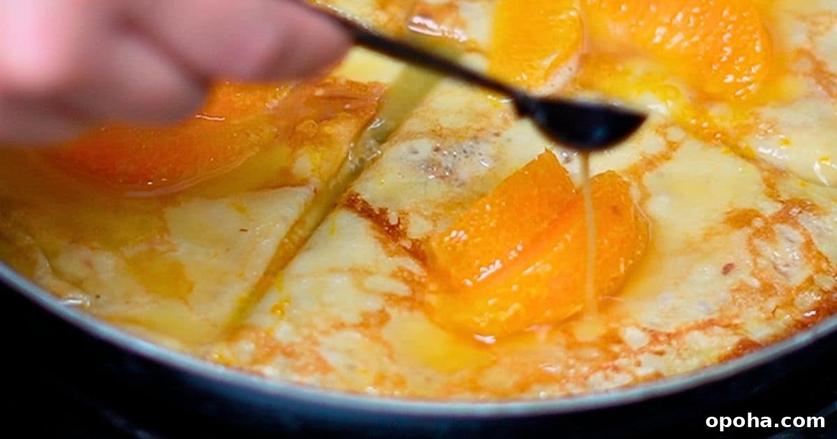 pouring hot orange butter sauce over crepes and orange slices in a skillet