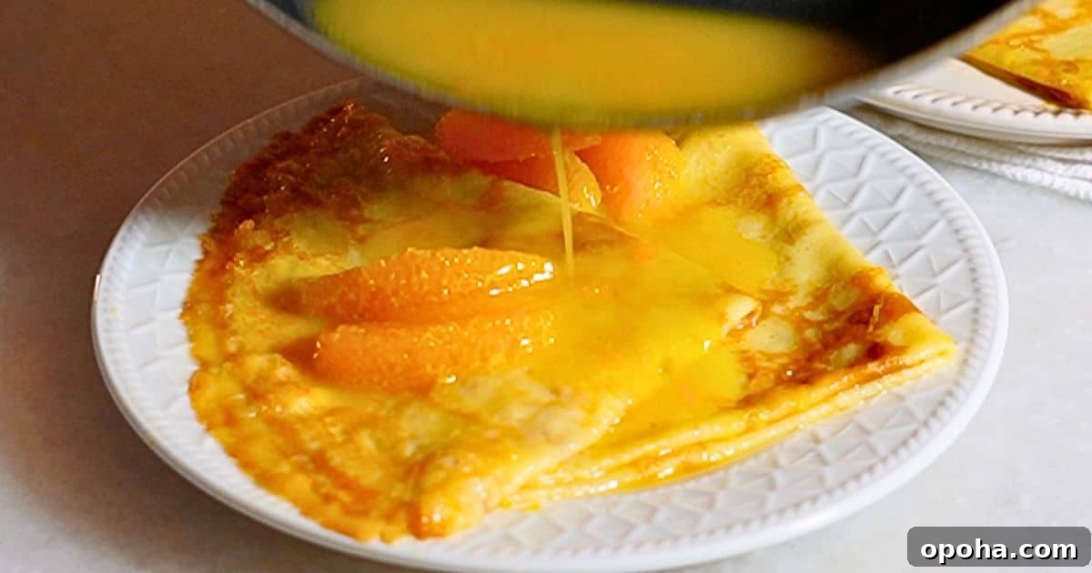 pouring hot orange butter sauce over homemade crepes on a plate