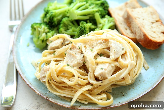 A serving of steamed broccoli, lemon chicken pasta, and two slices of crusty bread on a dinner plate with a fork on the left.