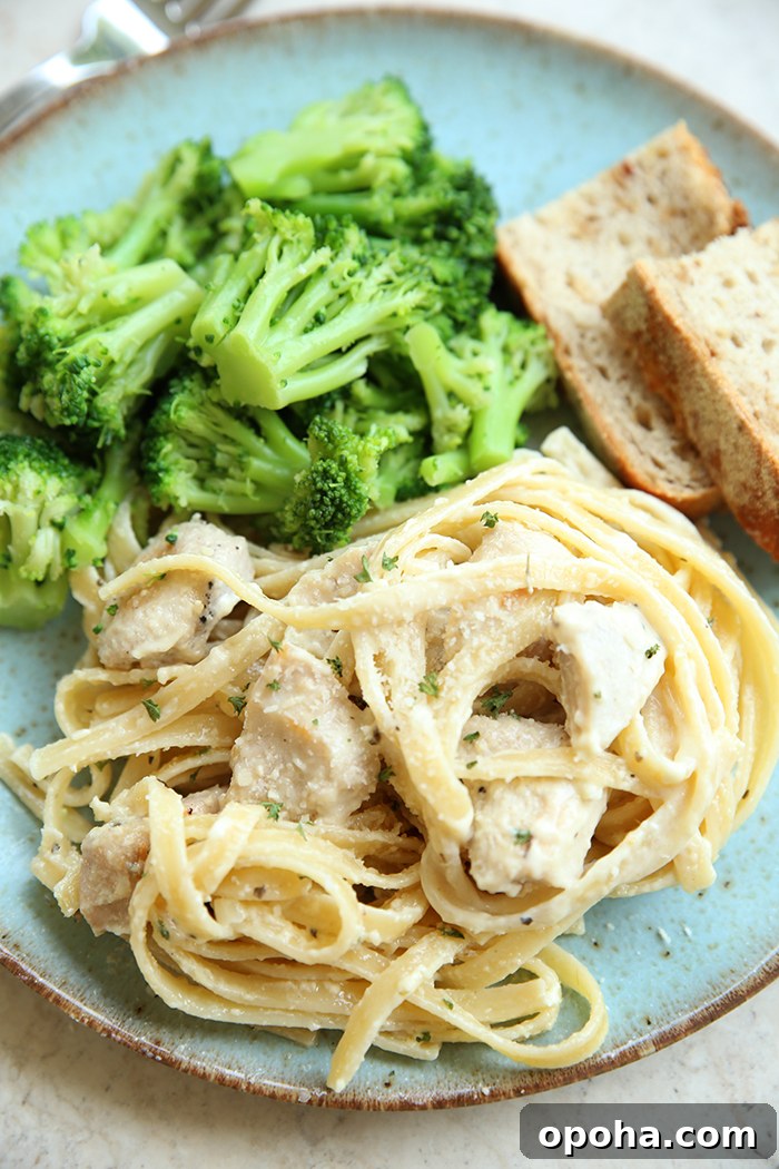A serving of lemon chicken fettuccini, broccoli, and two slices of ciabatta bread on a light blue plate.