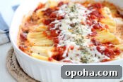 A white 9x13 oval baking dish filled with manicotti topped with red marinara sauce down the middle with mozzarella cheese and parsley on top sitting on a hot pad.