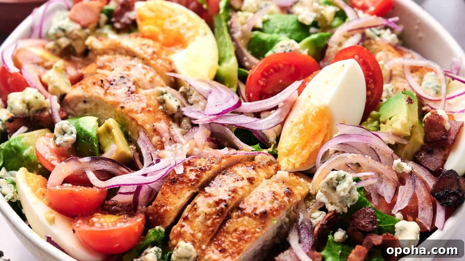 19 Summer Cookout Side Dishes I Make Every Weekend 11 A close-up of a Cobb salad featuring sliced chicken, cherry tomatoes, avocado, boiled eggs, red onion, bacon bits, and blue cheese crumbles on a bed of lettuce.