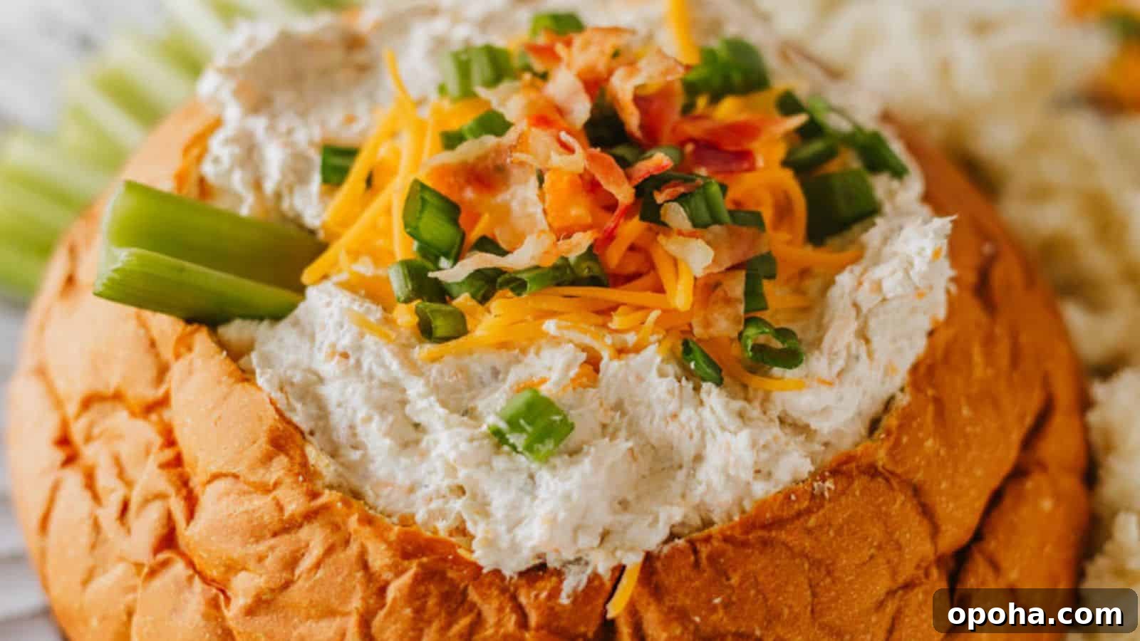 19 Summer Cookout Side Dishes I Make Every Weekend 6 A bread bowl filled with a creamy dip, garnished with shredded cheese, chopped green onions, and bacon bits. Celery sticks are placed on the side.