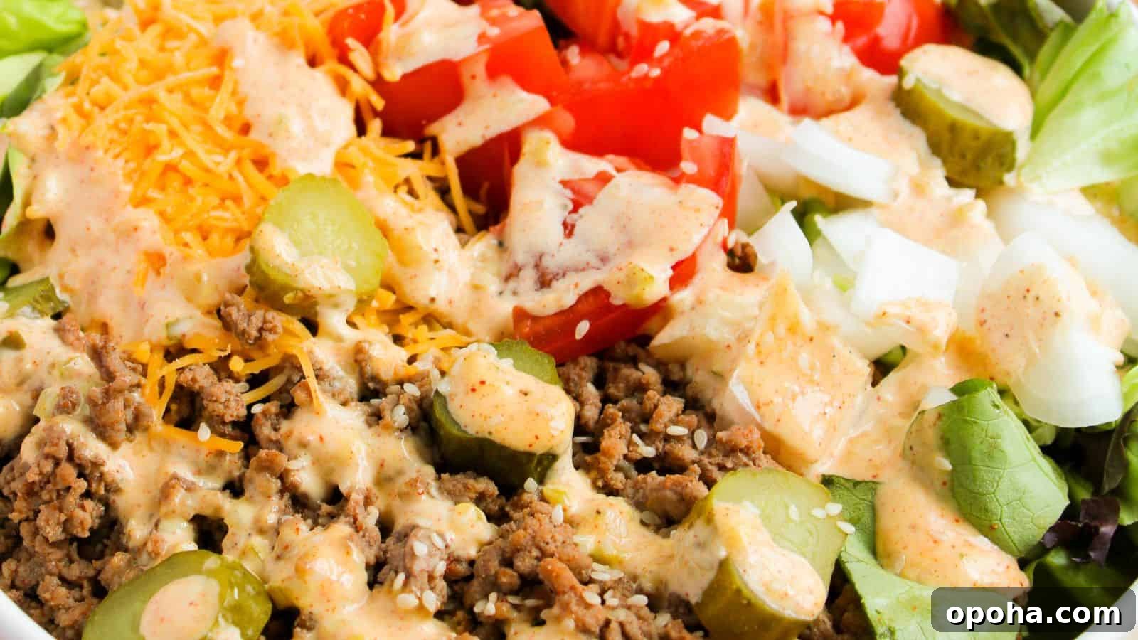 19 Summer Cookout Side Dishes I Make Every Weekend 9 Close-up of a salad featuring ground beef, sliced pickles, diced tomatoes, shredded cheese, and diced onions, topped with a creamy dressing.