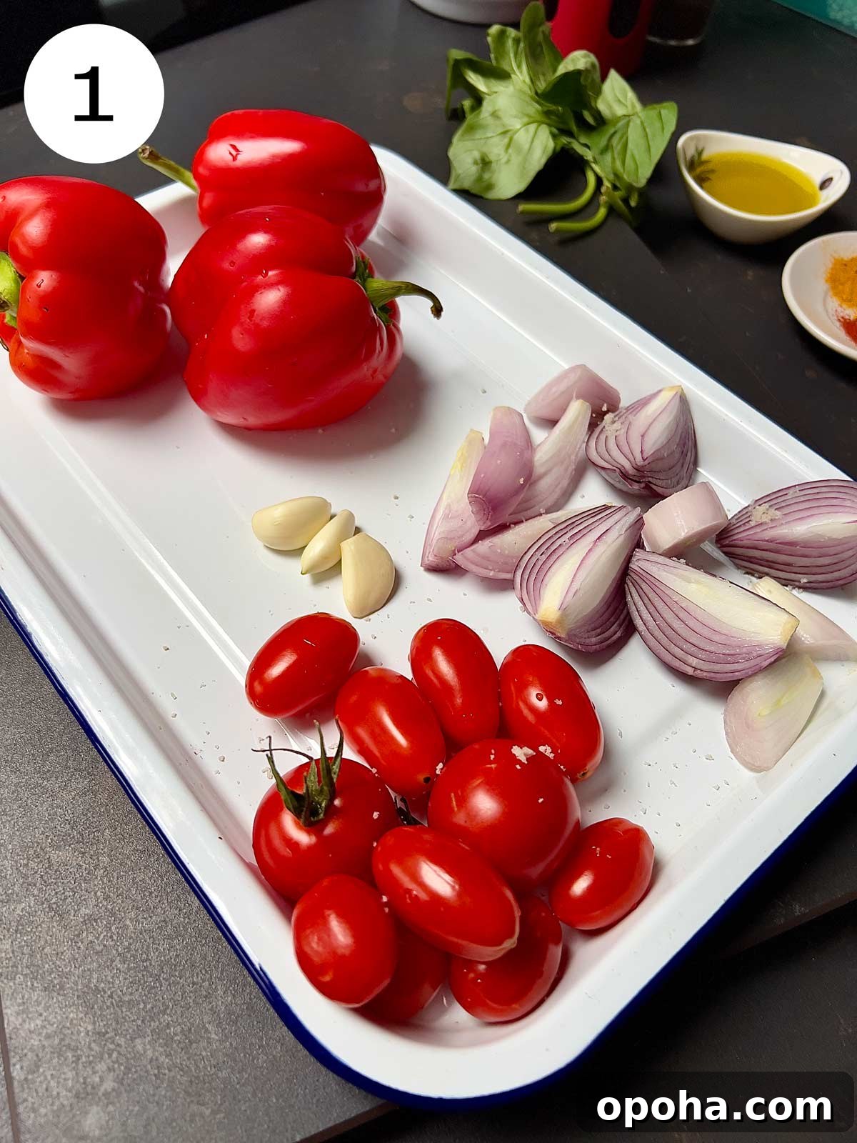 Onions cut into chunks, cherry tomatoes, garlic and 3 red bells peppers placed on a white enamel oven tray.