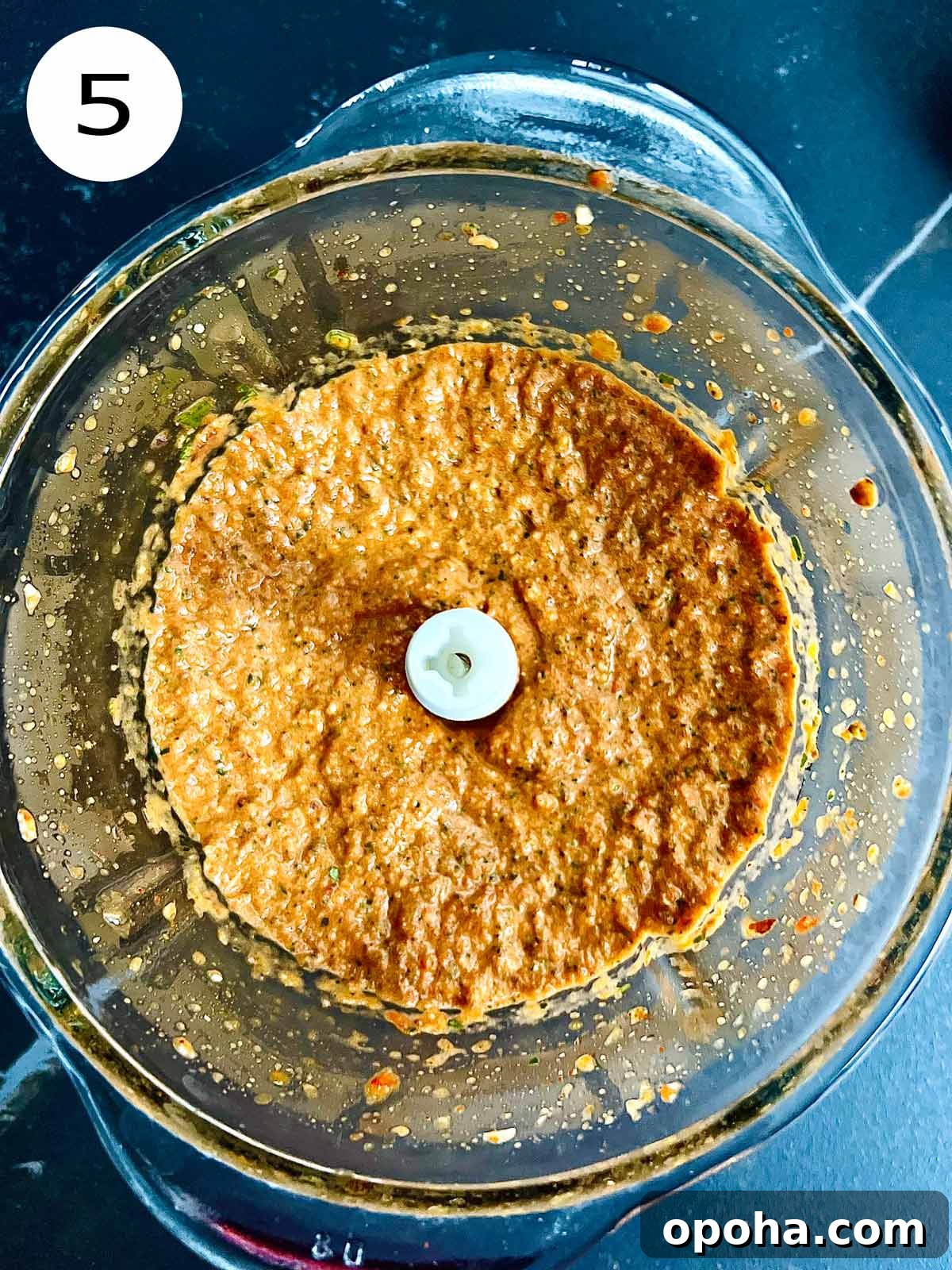 Roasted red bell pepper sauce ingredients blended in a coarse paste in a glass blender bowl.
