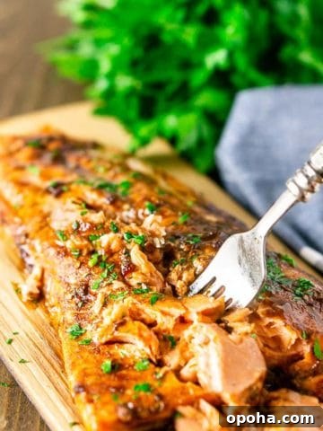 Maple-Chipotle Grilled Salmon on a wood plank, fork in salmon, parsley on table