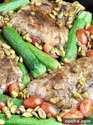 One pan dish containing salmon filets, baby zucchini, pistachios, and tomatoes.